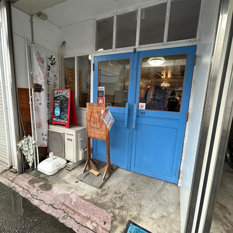 店の青いドアと看板に書かれた猫のイラストが、懐かしい商店街の雰囲気に溶け込んでいます。