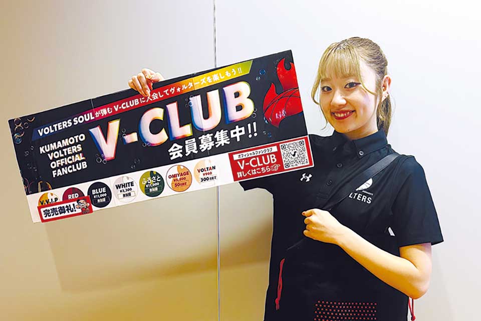 オフィシャルファンクラブ「V‐CLUB」のPRボードと会員限定グッズのバッグを持つチアリーダーのRIRIKAさん