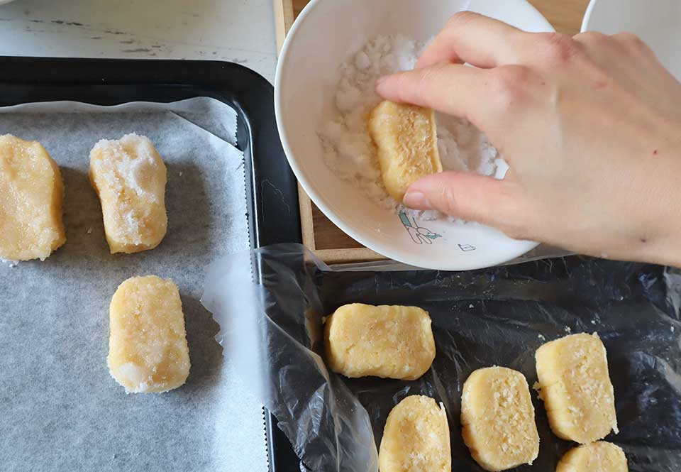 （5）のビニールを切り開き、生地を5～6mm幅にカットする。生地の縁を持ち、（6）の水に片面をサッとつけ、すぐに砂糖に押し付ける。砂糖の付いた面を上にして天板にのせていく。
